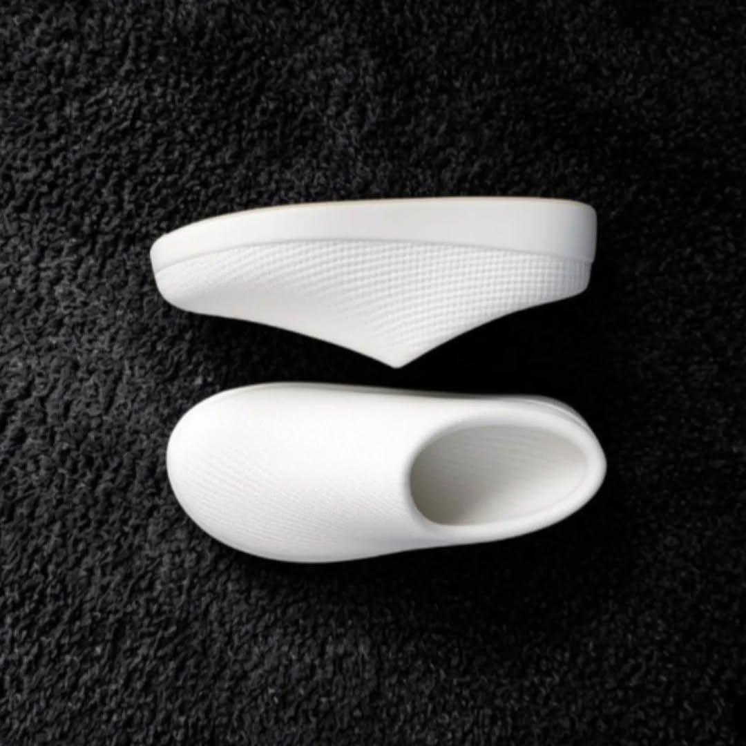 Pair of white Voronyz slip-ons on a black textured surface
